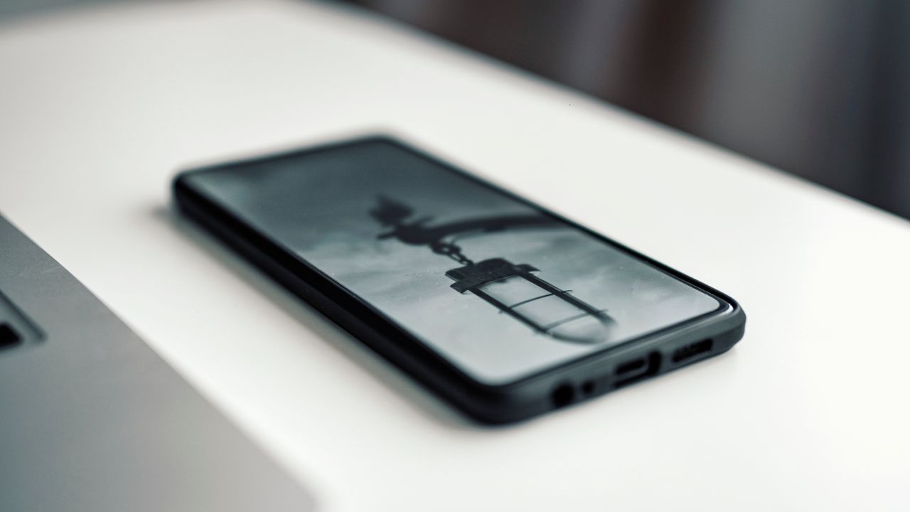 services-01 Close-up of a smartphone displaying a blurred image, placed on a desk beside a laptop.